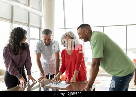 Femme d'affaires senior discutant sur le graphique avec des collègues qui se penchent sur le bureau Banque D'Images