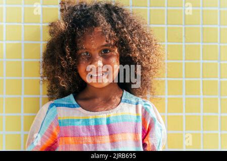 Fille souriante avec cheveux bouclés devant le mur jaune Banque D'Images