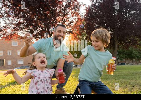 Enfants et père jouant avec des bulles au parc Banque D'Images