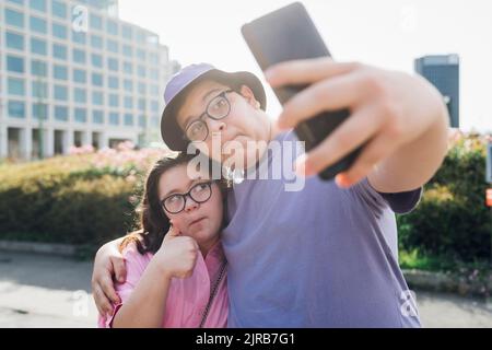 Jeune fille et garçon faisant des visages et prenant le selfie par téléphone mobile Banque D'Images