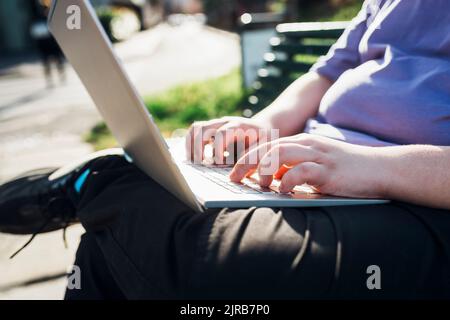 Mains d'un adolescent utilisant un ordinateur portable dans le parc Banque D'Images