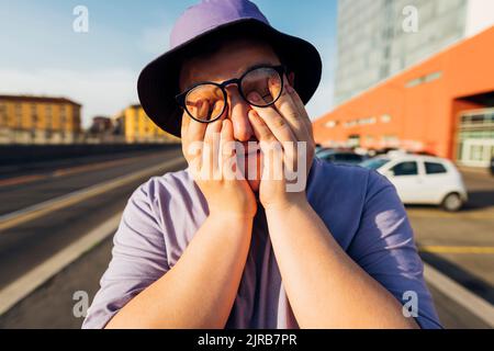 Adolescent couvrant le visage avec les mains le jour ensoleillé Banque D'Images