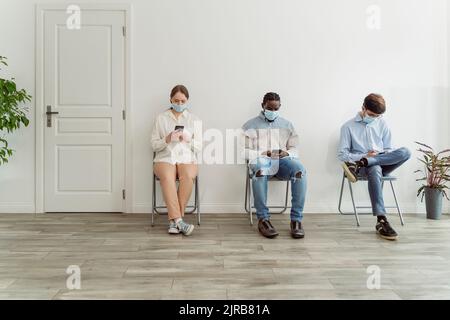 Les personnes portant un masque facial assis sur des chaises dans la salle d'attente Banque D'Images