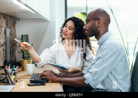 Femme d'affaires pointant sur un écran d'ordinateur assis par un homme d'affaires au bureau Banque D'Images