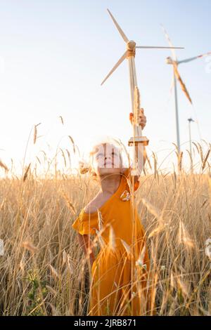 Fille jouant avec le modèle d'éolienne dans le champ de blé Banque D'Images