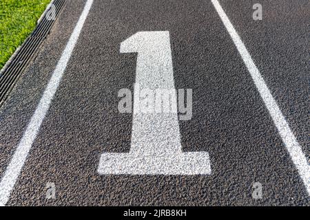 Gros plan sur la voie numéro un, 1, sur une nouvelle piste de course noire avec des lignes de voie blanches et d'autres marquages. Banque D'Images