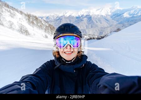 Femme souriante portant des lunettes de ski devant des montagnes enneigées Banque D'Images