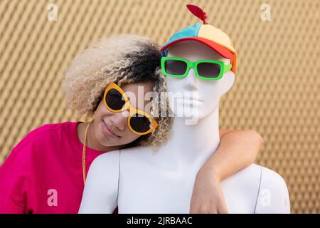 Femme souriante avec mannequin portant des lunettes de soleil devant le mur Banque D'Images