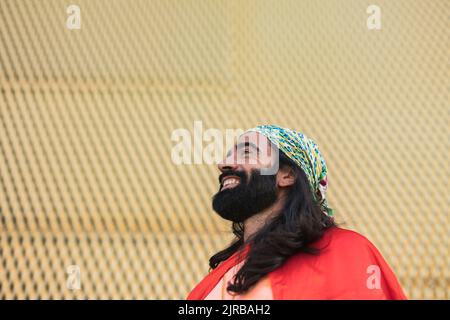 Joyeux homme barbu avec de longs cheveux noirs devant le mur Banque D'Images