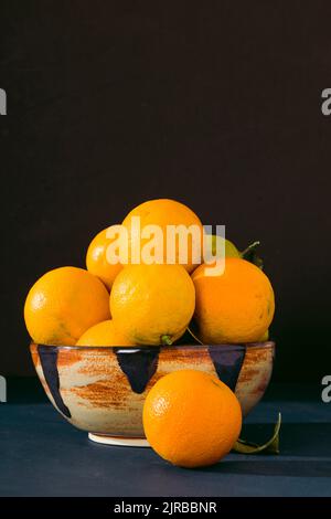 Bol en céramique rempli d'oranges Valencia fraîches sur fond noir Banque D'Images