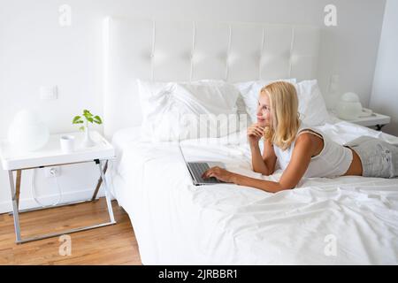 Thoughtful woman lying on bed at home Banque D'Images