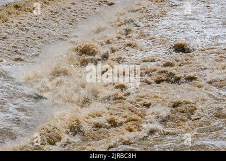 Rapides sur la rivière après une forte pluie en saison des pluies. L'eau boueuse se déplace avec une grande rapidité en passant au-dessus d'un déversoir, tombant, éclaboussant et formant Banque D'Images