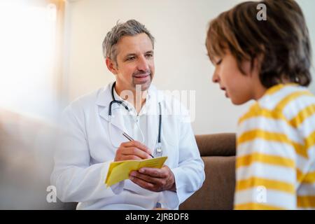 Médecin avec un garçon à la maison écrivant dans la passe de vaccination Banque D'Images