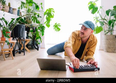 Homme souriant pratiquant le piano allongé sur le sol à la maison Banque D'Images