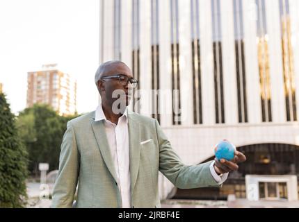 Homme d'affaires mature avec figurine globe debout devant le bâtiment Banque D'Images