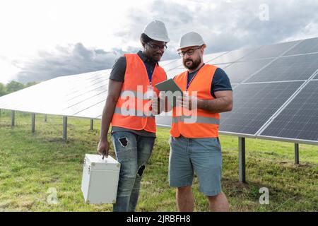 Les ingénieurs multiraciaux discutent sur un PC tablette à la station solaire Banque D'Images