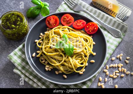 Pâtes italiennes traditionnelles aux légumes frais, parmesan, feuilles de basilic, pignons et sauce pesto, servies dans une assiette noire sur le backgro en pierre grise Banque D'Images