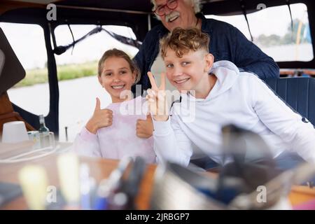 Homme âgé avec petits-enfants faisant des gestes positifs dans le bateau Banque D'Images