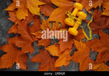 Deux haltères jaunes avec mètre à ruban (ou mètre à ruban) sur les feuilles d'automne. Composition de la mise en place de la salle de gym, concept d'automne sain de style de vie de forme physique Banque D'Images
