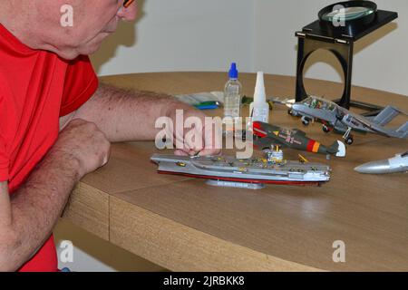 kit de modèle en plastique, homme avec des lunettes utilisant des pinces dans le kit de modèle en plastique utilisant des pinces pour l'assemblage, à la maison dans la pandémie, avec viseur et mavif Banque D'Images