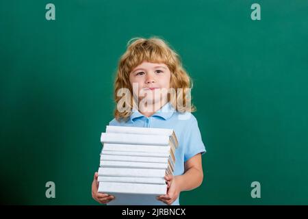 Un enfant heureux contre un tableau noir vert. Concept d'éducation et de créativité. Pile de livres avec plaque de mortier sur tableau noir. Retour à l'école Banque D'Images