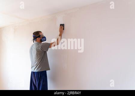 Cliché sélectif de l'homme avec équipement de sécurité ponçant le mur avec du papier de verre. Il y a un espace de titre au cadre. Banque D'Images