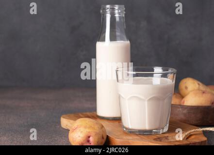 Le lait de pomme de terre vegan en bouteille et en verre, ainsi que les pommes de terre dans une assiette sur fond gris. Produit de remplacement du lait sans lactose à base de plantes Banque D'Images