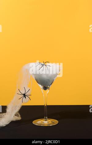 Mise en page créative en verre martini, toile d'araignée et araignées sur fond ocre et noir. Concept de fête d'Halloween. Copier l'espace. Banque D'Images