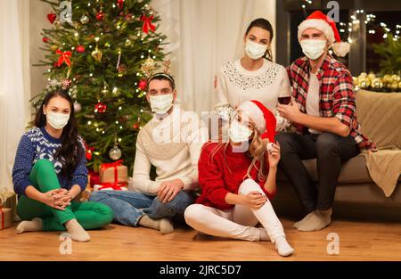 des amis dans des masques qui boivent du vin à noël Banque D'Images
