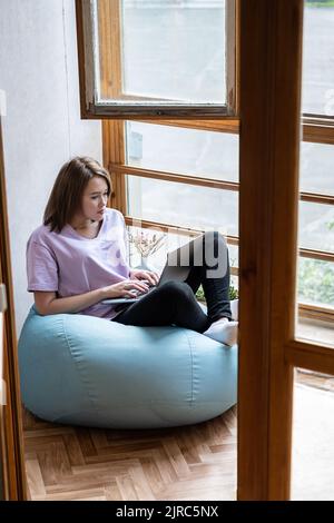 Jeune femme utilisant un ordinateur portable sur un balcon ensoleillé. Travail à domicile, concept indépendant. Banque D'Images