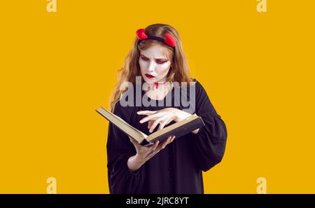 Jeune femme habillée dans le costume effrayant Halloween lecture livre de sorts de magie de mal Banque D'Images