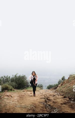 Jeune femme latine plus taille avec sac à dos, escalade d'une colline et randonnée dans un beau paysage. Verticale Banque D'Images