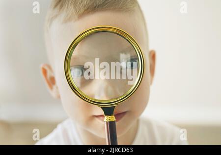 Visages d'un garçon tenant une loupe dans sa main et regardant joyeusement dans la caméra à travers elle. Gros plan. Banque D'Images