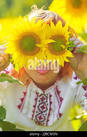 fille en broderie hid les yeux derrière les tournesols. Femme heureuse parmi les fleurs jaunes. Le jour de l'indépendance de l'Ukraine. Vêtements nationaux de l'Ukraine. Banque D'Images