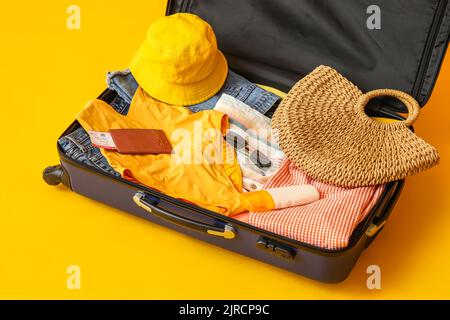 Valise avec vêtements, accessoires de plage, billet et passeport sur fond jaune Banque D'Images