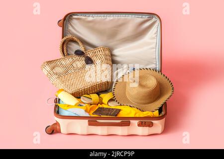 Valise avec vêtements, accessoires de plage et passeport sur fond rose Banque D'Images