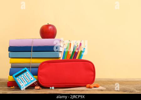 Étui à crayons rouge avec papeterie scolaire et pomme sur table sur fond beige Banque D'Images