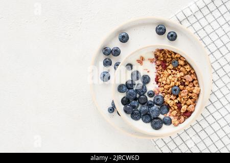 Bol de yaourt maison avec granola et myrtilles sur fond clair. Vue de dessus, espace de copie pour le texte Banque D'Images