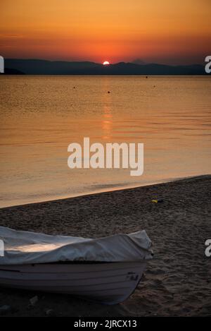 Soleil levant sur les montagnes de Sithonia, vue de Kassandra à Halkidiki Grèce. Le bateau est couvert sur la plage. Banque D'Images