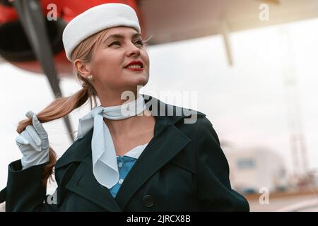 Femme de bord en uniforme debout près de l'avion à l'aéroport et regardant loin Banque D'Images