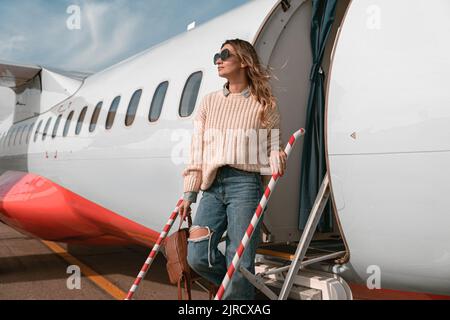 Femme passager dans des lunettes de soleil debout sur les escaliers d'avion à l'aéroport et regardant loin Banque D'Images