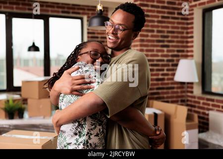 Un mari et une femme joyeux partageant un câlin et appréciant la réinstallation de la propriété, ayant un moment romantique après avoir déménagements dans une nouvelle maison ensemble. Embrasser et célébrer l'événement de vie dans l'appartement loué. Banque D'Images