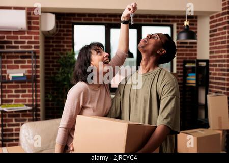 Femme excitée tenant les clés de la maison pour se déplacer dans l'appartement après avoir acheté une nouvelle maison familiale pour l'avenir. Les propriétaires célébrant l'événement de vie et la réalisation de la relation, la réinstallation à la maison. Banque D'Images