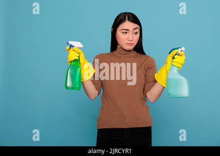 Portrait de jeune femme de ménage asiatique frustrée et triste au travail tenant deux spray détergent, concept de maison de nettoyage, enfoncé submergé et négatif en raison du travail excessif de jour en jour corvées Banque D'Images