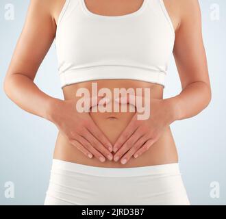 Maintien de la forme jusqu'à son noyau. Court studio photo d'une jeune femme en forme avec ses mains encadrant son estomac sur un fond gris. Banque D'Images