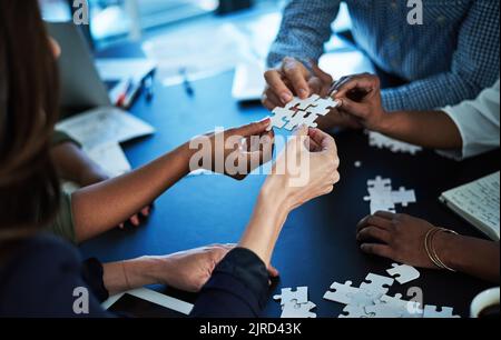 Toutes les pièces sont réunies. Un groupe de collègues non identifiables construisant un puzzle ensemble à une table dans la salle de conférence. Banque D'Images