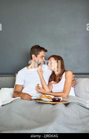 Réveillez-vous, puis dégustez du vin et dînez. Un jeune couple heureux prenant le petit déjeuner au lit à la maison. Banque D'Images