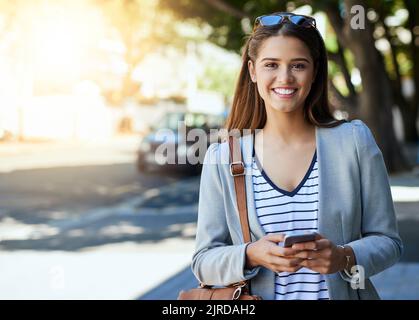 Connecté en déplacement. Portrait court d'une jeune femme attrayante utilisant son téléphone portable lors de ses déplacements au travail. Banque D'Images