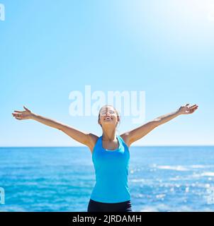 Courir me connecte à mon corps. Une jeune femme sportive debout avec ses bras étendus sur la plage. Banque D'Images