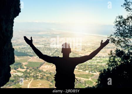 Entouré par la beauté naturelle et un paysage à couper le souffle. Vue arrière d'un jeune homme debout au sommet d'une montagne avec ses bras étirés. Banque D'Images